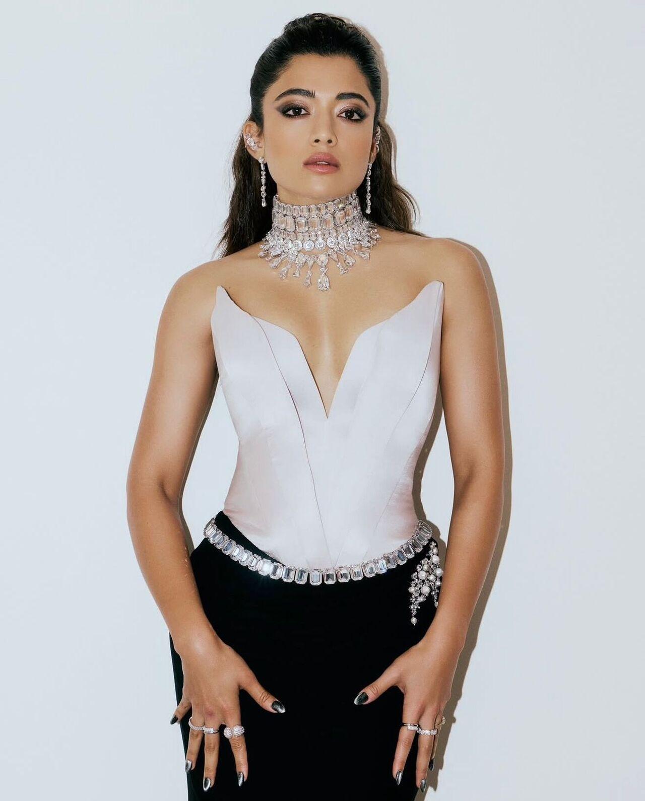 Turning heads in a sleek black skirt and structured white corset top, Rashmika exudes high-fashion confidence. The bold neckline, diamond choker, and powerful stance make this a striking, red-carpet-ready moment